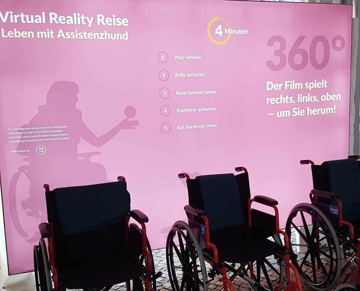Fotowand Virtual Reality Reise :: Auf dem Foto sieht man die Fotowand Virtual Reality Reise,der Assistenzhunde Ausstellung.
Vor der Fotowand stehen drei Rollstühle.
