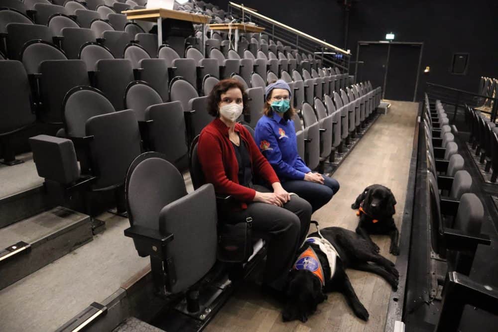 Dr. Hannah Reuter mit Blindenführhündin Daika und Julia mit Assistenzhündin Samu sitzen im Düsseldorfer Schauspielhaus Saal.
