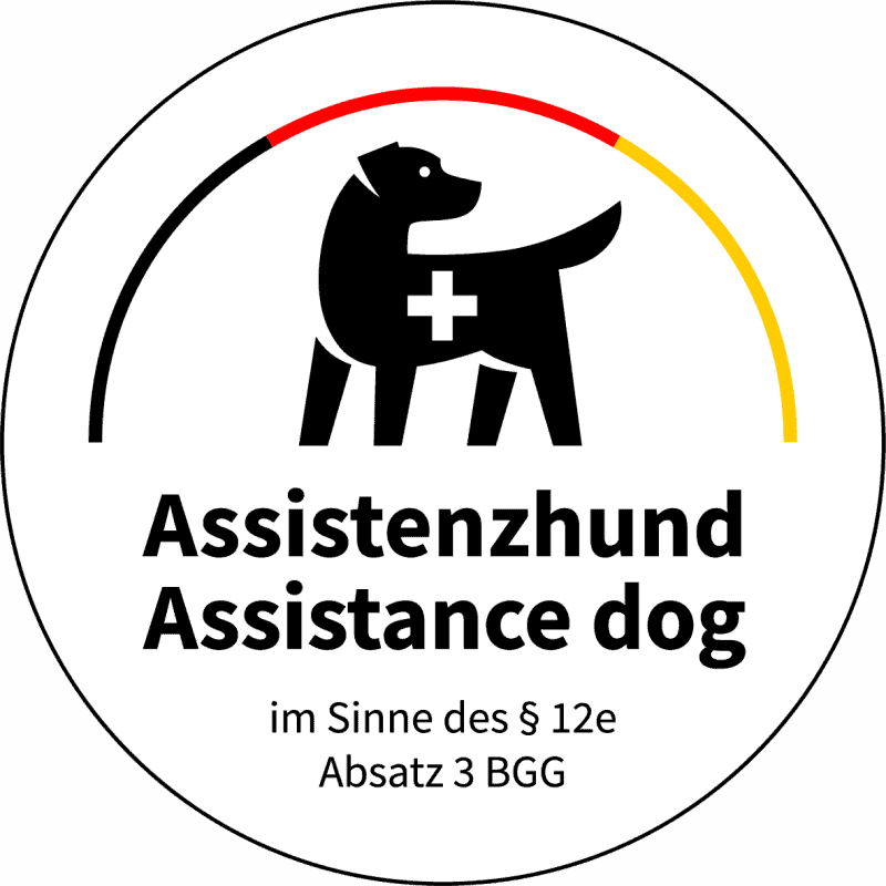 Das neue staatliche Kennzeichen von Deutschlands Assistenzhundgesetz ist weiß und rund. Ein aufmerksamer, schwarzer Hund im Seitenprofil wird durch ein großes, weißes Kreuz am Torso als Assistenzhund identifiziert. Über ihm, regenbogenartig, die Farben schwarz-rot-gold. Darunter der Text - "Assistenzhund, assistance dog, im Sinne des § 12e Absatz 3 BGG".