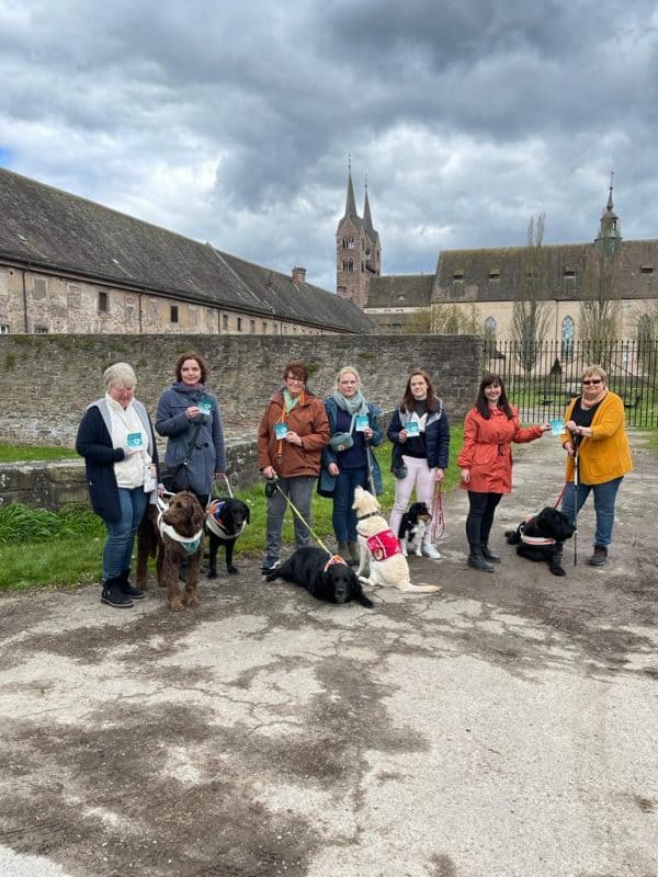 Im Vordergrund halten viele Menschen den "Assistenzhund willkommen" Aufkleber hoch, im Hintergrund ist Schloss Corvey