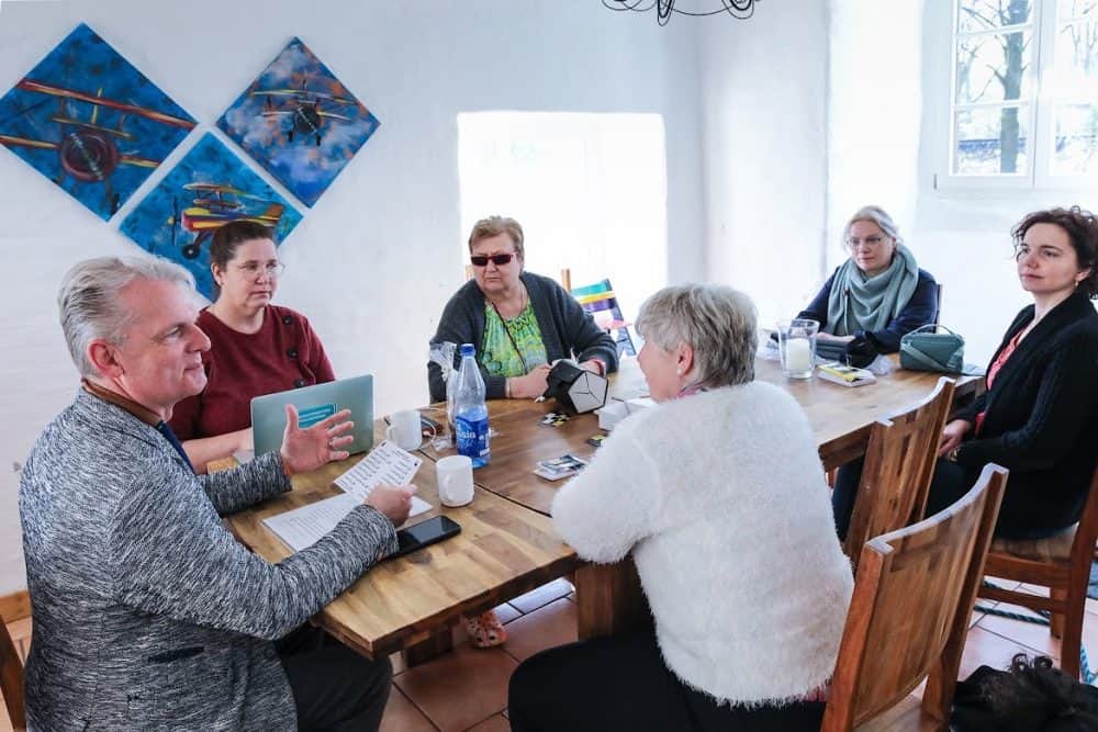 An einem großen Tisch sitzen sechs Personen und arbeiten