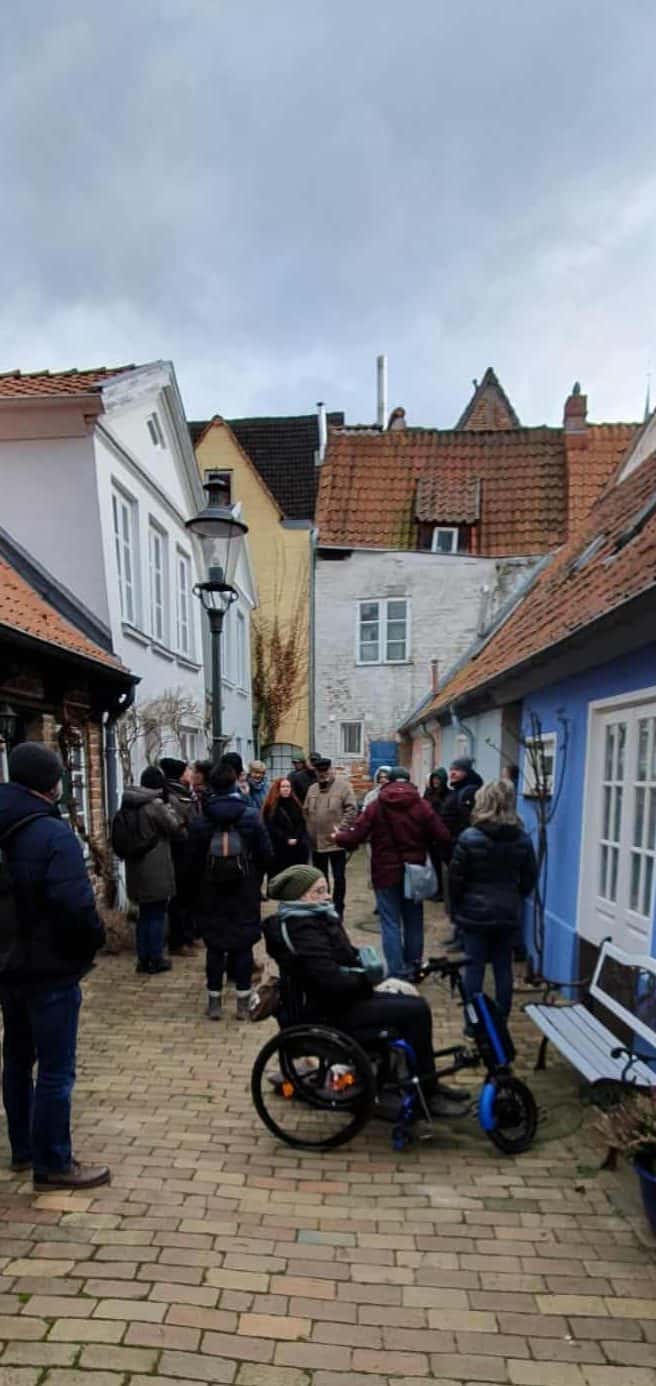 In einem engen Hof steht eine Gruppe von menschen, darunter eine Frau im Rolli mit Assistenzhund