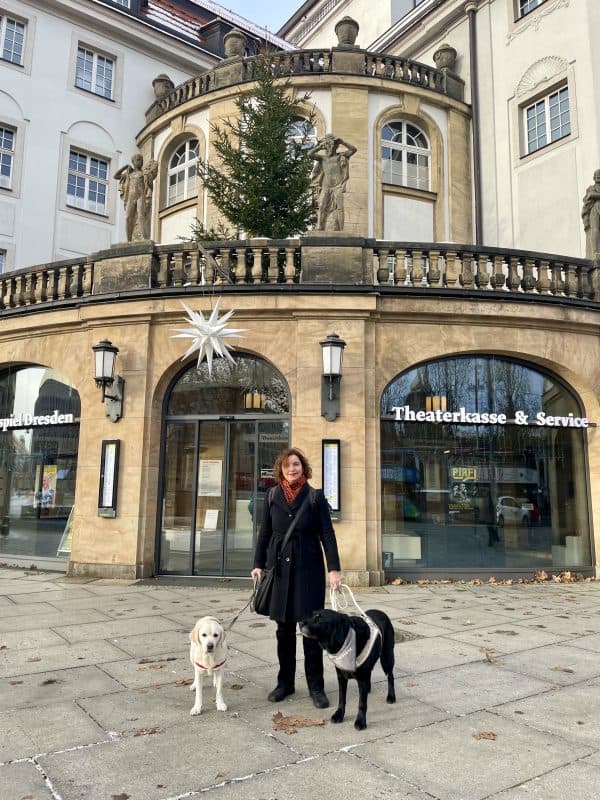 Dr. Hannah Reuter steht mit Daika und Mascha vor dem historischen Gebäude des Staatsschauspiels Desden.